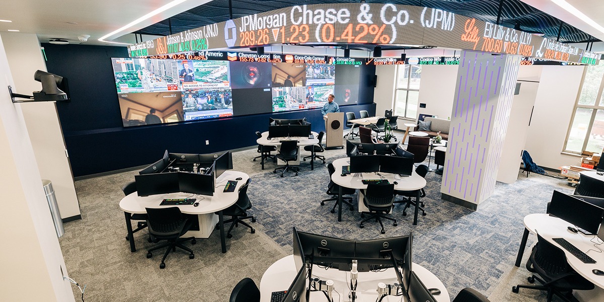 business classroom with computers, wall of TVs, and stock ticker going across the ceiling